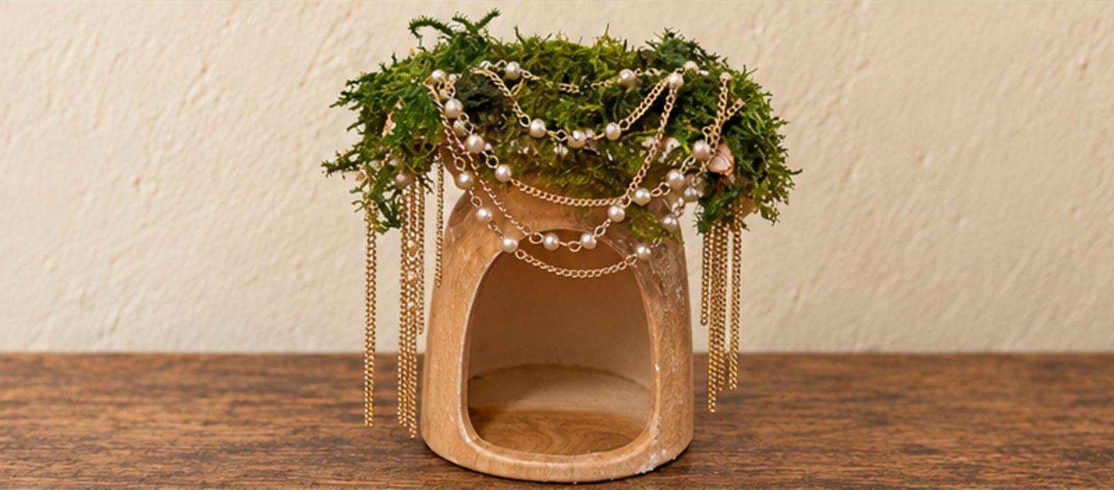 The redesigned fairy house with a moss roof and draped pearl and gold chains