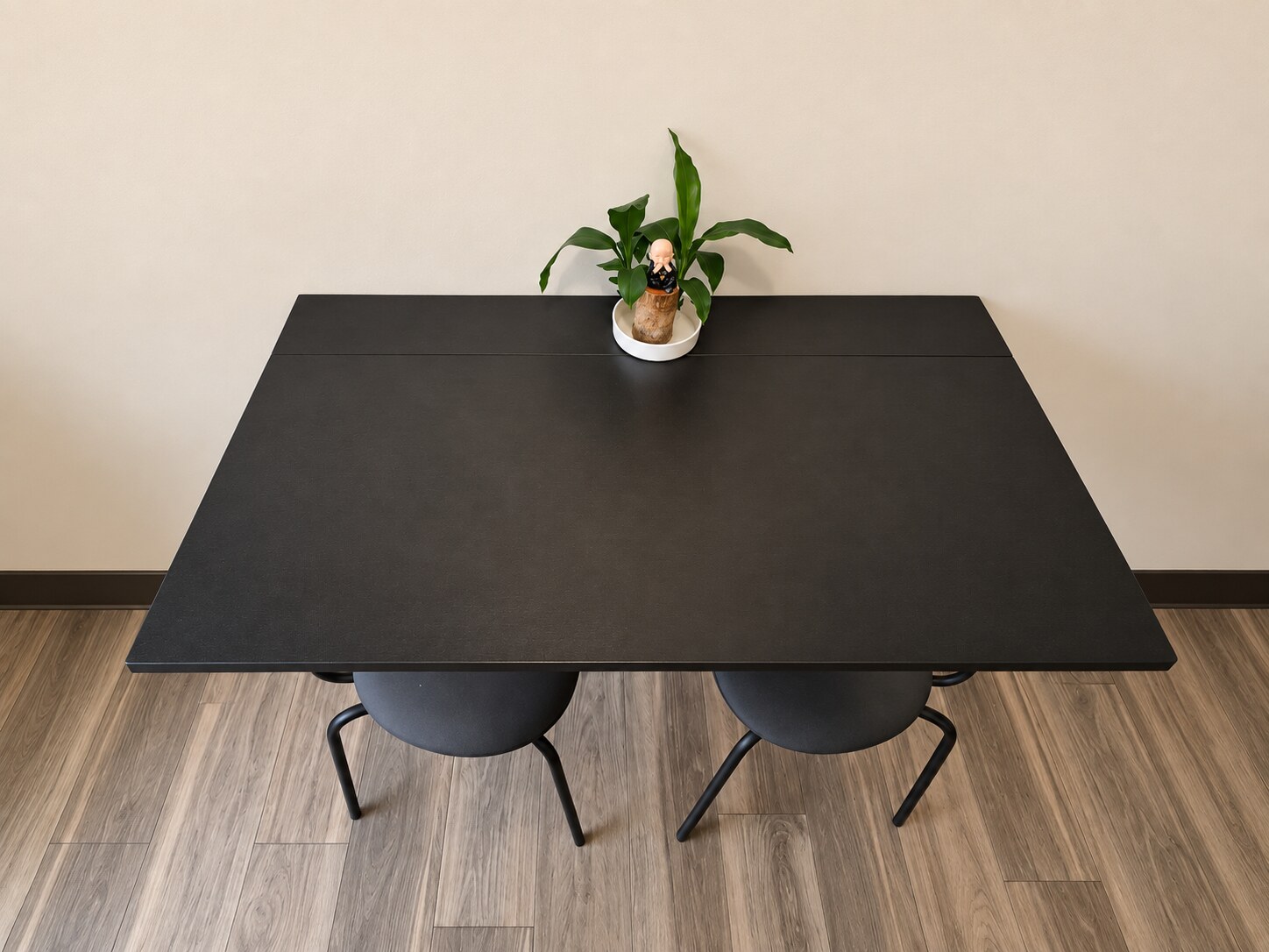 A black wall-mounted folding table with two low-backed chairs tucked beneath it