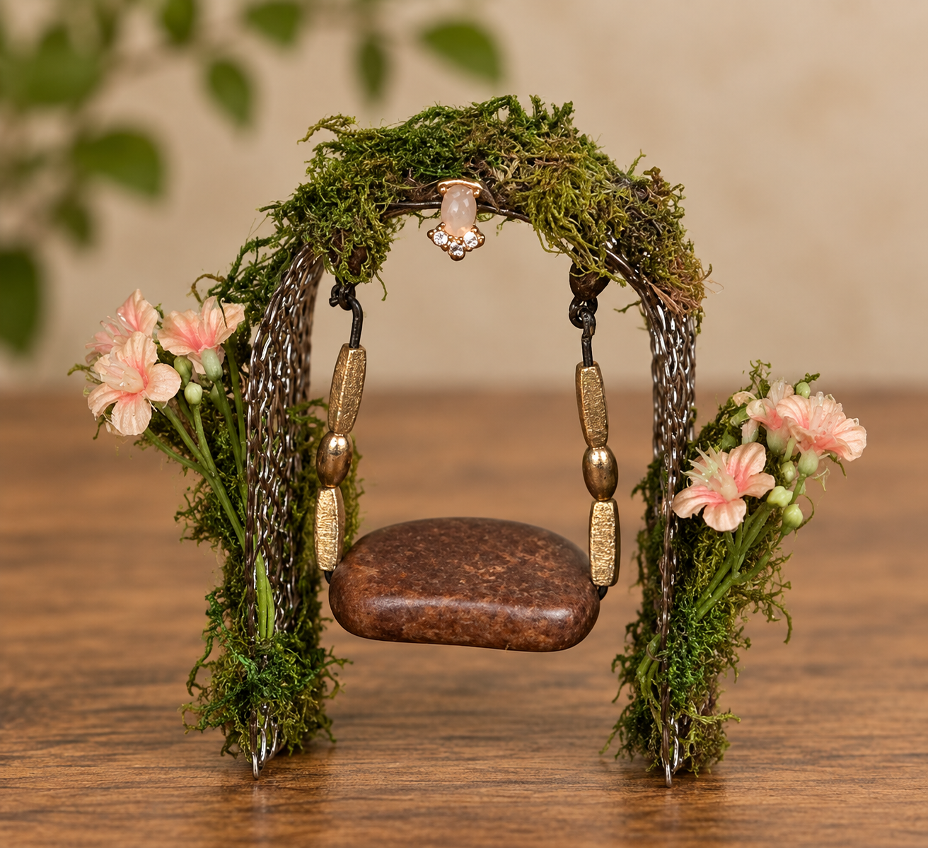 A finished miniature fairy swing made from decorative metal ribbon, thrifted jewelry, moss, and pink flowers
