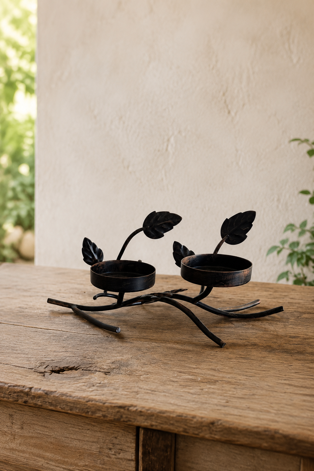 A black iron two-tier candle stand with leaf and branch details